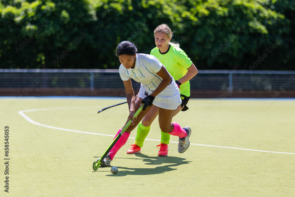 Two female field hockey players fighting for the ball on the pitch in attack