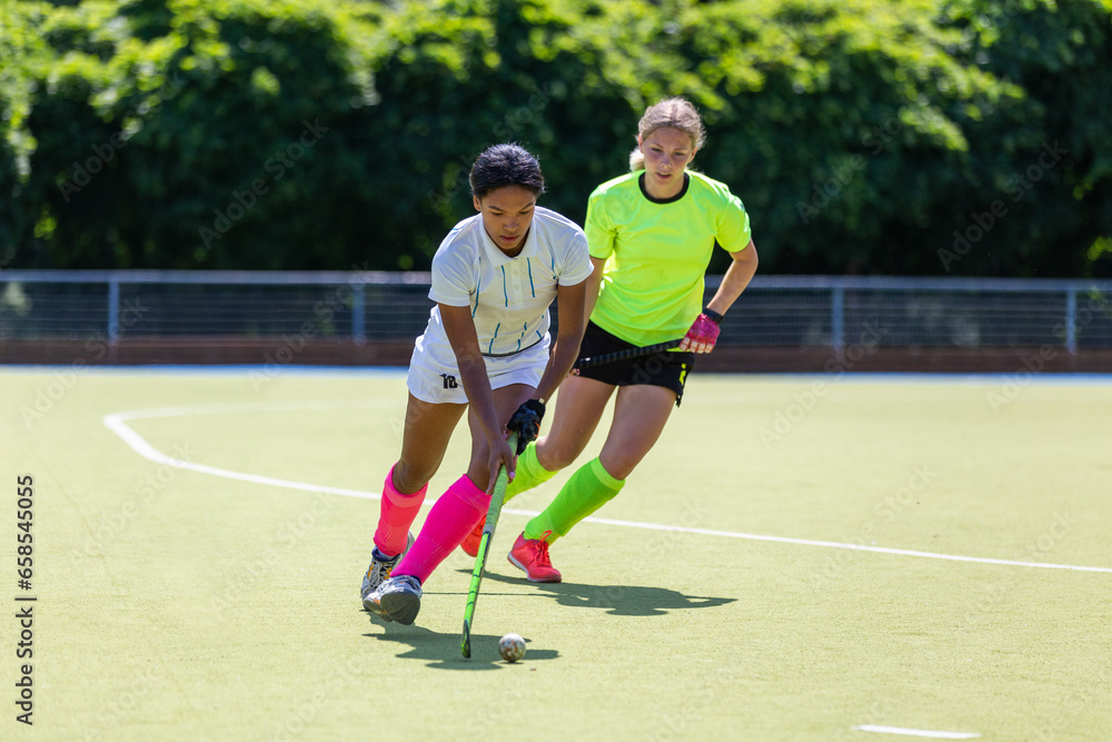 Two female field hockey players fighting for the ball on the pitch in attack