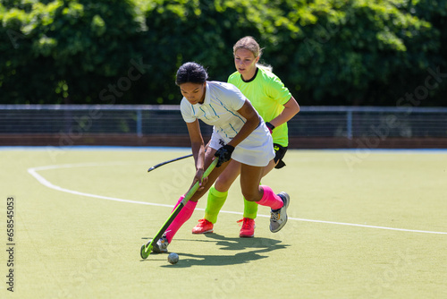 Two female field hockey players fighting for the ball on the pitch in attack © skumer