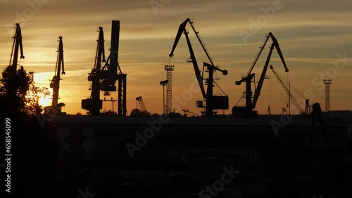 A panorama of cranes silhouetted against a sunset sky in Ventspils shipyard