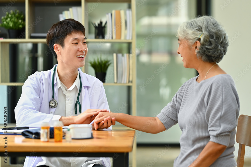 Obraz premium Smiling doctor in white coat holding hand, supporting senior female patient. Medical healthcare concept