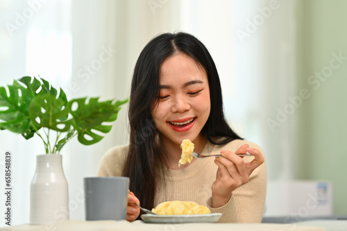 Happy young asian woman in casual clothes having breakfast at home. Concept of wellness, food and domestic lifestyle