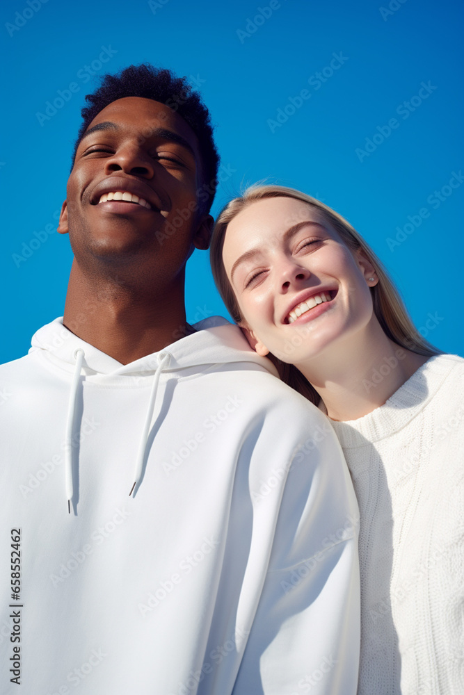 An unknown Black man and an unknown white-skinned woman in white sweatshirts smile on a blue background An unknown Black man and an unknown white-skinned woman in white sweatshirts smile on a blue background