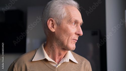 Fotografia A pensive elderly man standing near window and thinking about retirement, proble