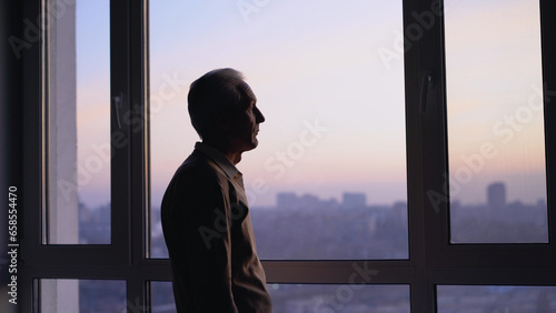 An unhappy elderly man looking out the window, feeling lonely in the city, haunted by sad memories