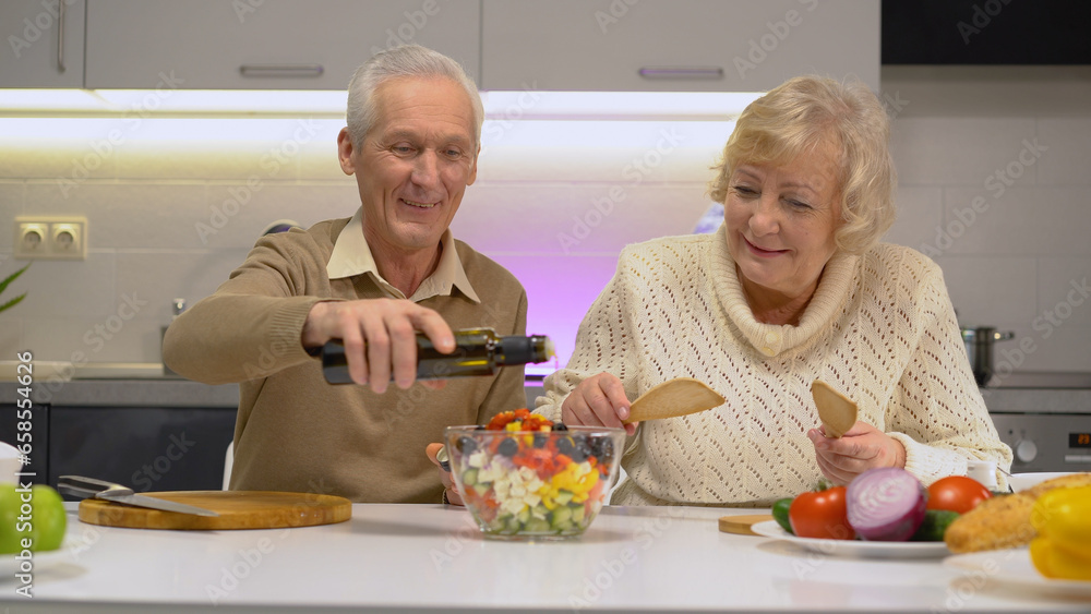 A mature man pouring olive oil into a bowl with fresh vegetable salad, seasoning it, couple cooking together A mature man pouring olive oil into a bowl with fresh vegetable salad, seasoning it, couple cooking together