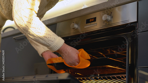 A woman taking a hot baking pan from the oven, using safe silicone mitts during her cooking hobby photo