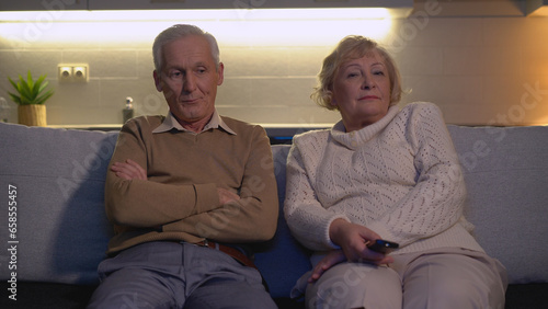 Fotografi An offended man and woman are sitting at home on the sofa in front of the TV, re