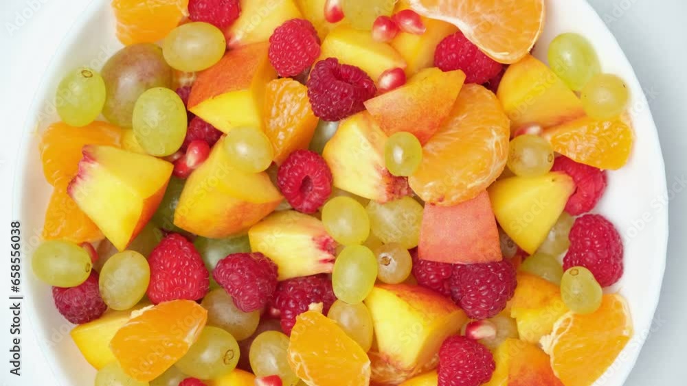 A person takes a berry from a fruit salad from an assortment of fruits and berries. A person takes a berry from a fruit salad from an assortment of fruits and berries.