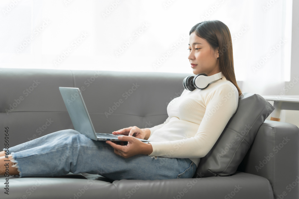 Asian woman with braces sits online shopping on sofa with laptop. mobile phone and credit card in hand Asian woman with braces sits online shopping on sofa with laptop. mobile phone and credit card in hand