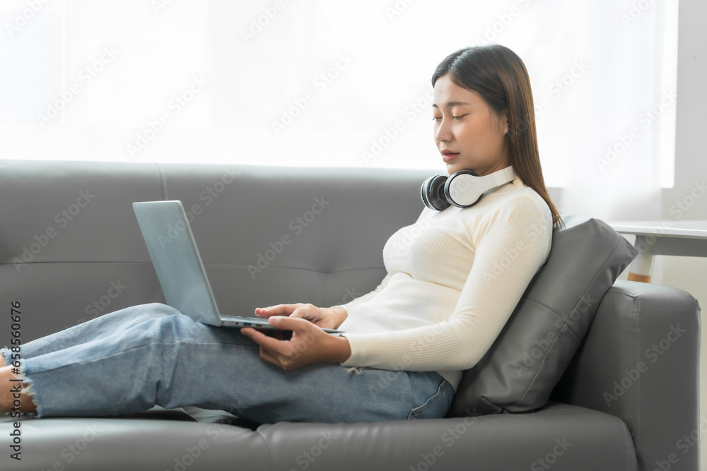 Asian woman with braces sits online shopping on sofa with laptop. mobile phone and credit card in hand Asian woman with braces sits online shopping on sofa with laptop. mobile phone and credit card in hand