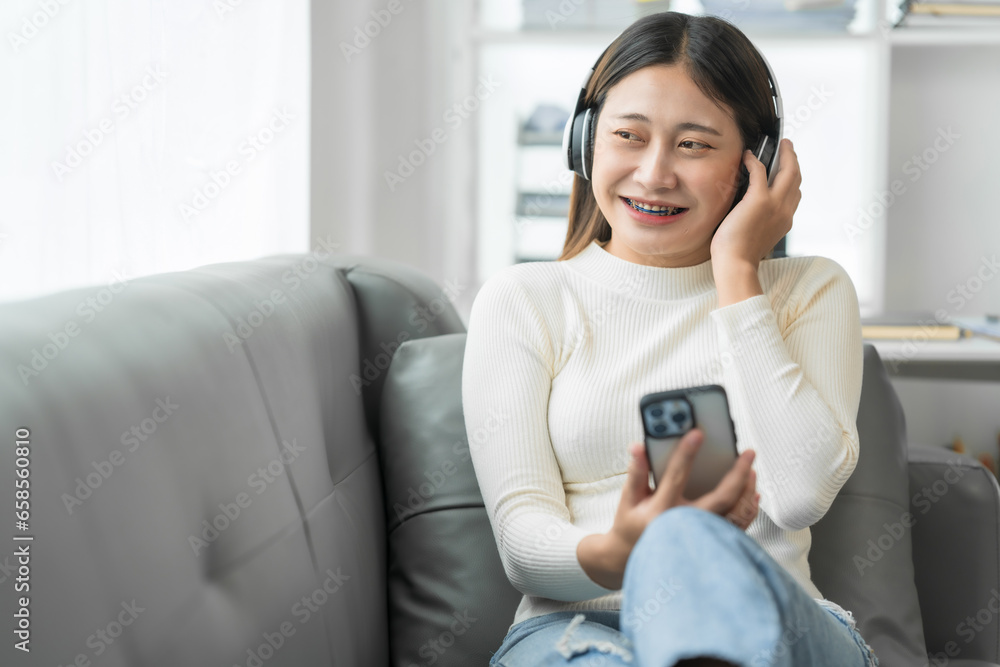 Asian woman with braces sits online shopping on sofa with laptop. mobile phone and credit card in hand