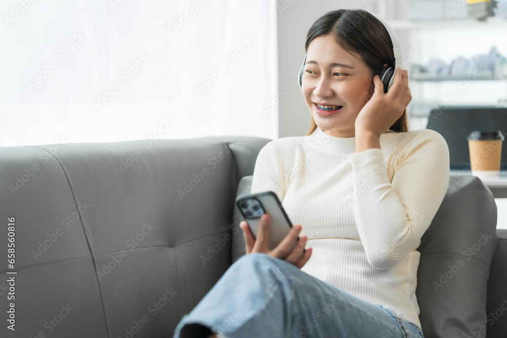 Asian woman with braces sits online shopping on sofa with laptop. mobile phone and credit card in hand Asian woman with braces sits online shopping on sofa with laptop. mobile phone and credit card in hand