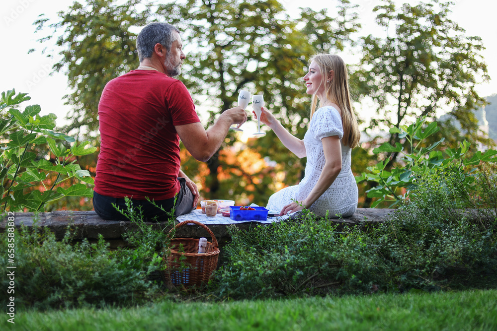 Obraz premium couple sitting with wine glasses and having fun talking at backyard on a sunset. Spending summer time and having a party outdoors