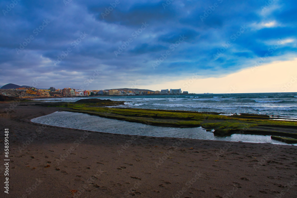 Tranquil Dawn: El Médano's Golden Hour with Waves, Rocks, and Sand