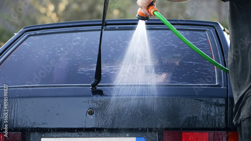 water from a hose from a spray bottle washes the car. Car washes use high pressure water sprays, detergents. washes the car at home in the garage. black car rear view photo