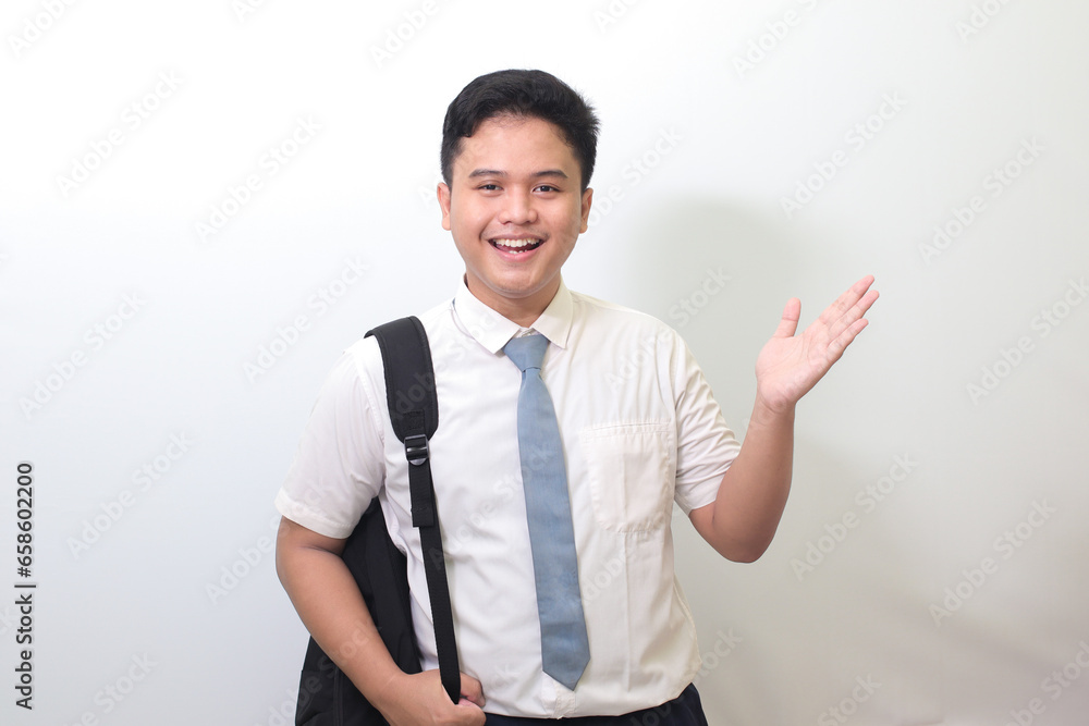 Indonesian senior high school student wearing white shirt uniform with gray tie showing product, pointing at something and smiling. Isolated image on white background Indonesian senior high school student wearing white shirt uniform with gray tie showing product, pointing at something and smiling. Isolated image on white background