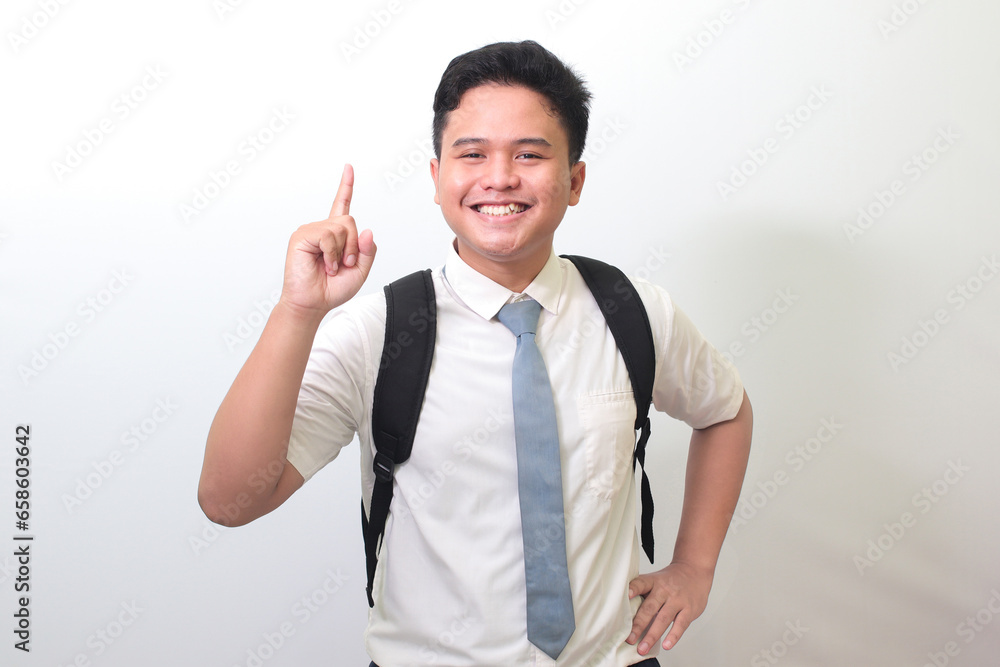 Indonesian senior high school student wearing white shirt uniform with gray tie pointing up with finger and reminding something to do. Isolated image on white background Indonesian senior high school student wearing white shirt uniform with gray tie pointing up with finger and reminding something to do. Isolated image on white background