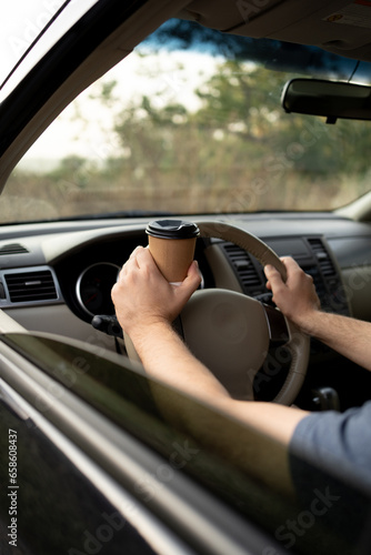Young man driving holding a paper coffee cup, close-up. Takeaway drink. Busy man with a cup of coffee in car © mtrlin