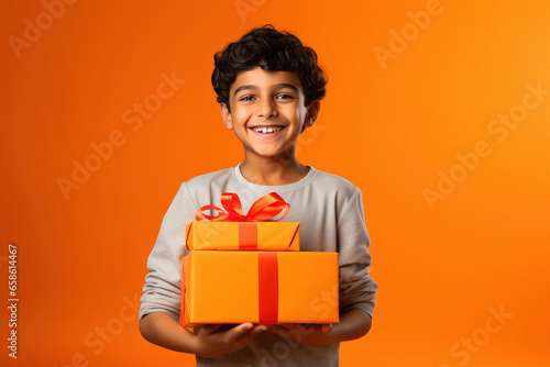 Indian little boy holding gift box in hand on yellow background. © Niks Ads