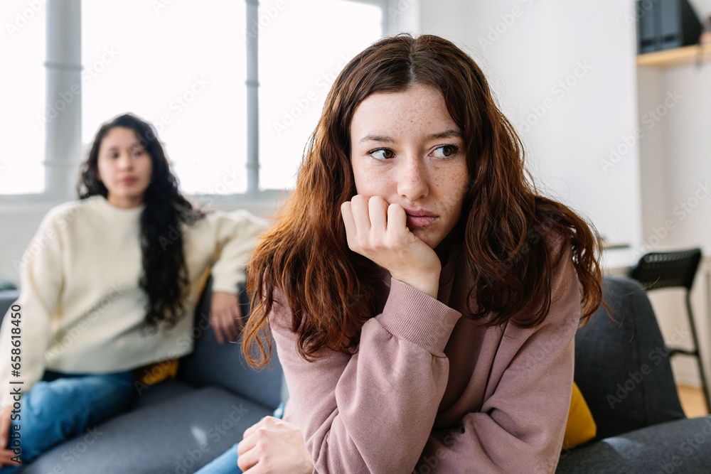 Two angry female friends sitting separately on sofa at home after an argument Two angry female friends sitting separately on sofa at home after an argument