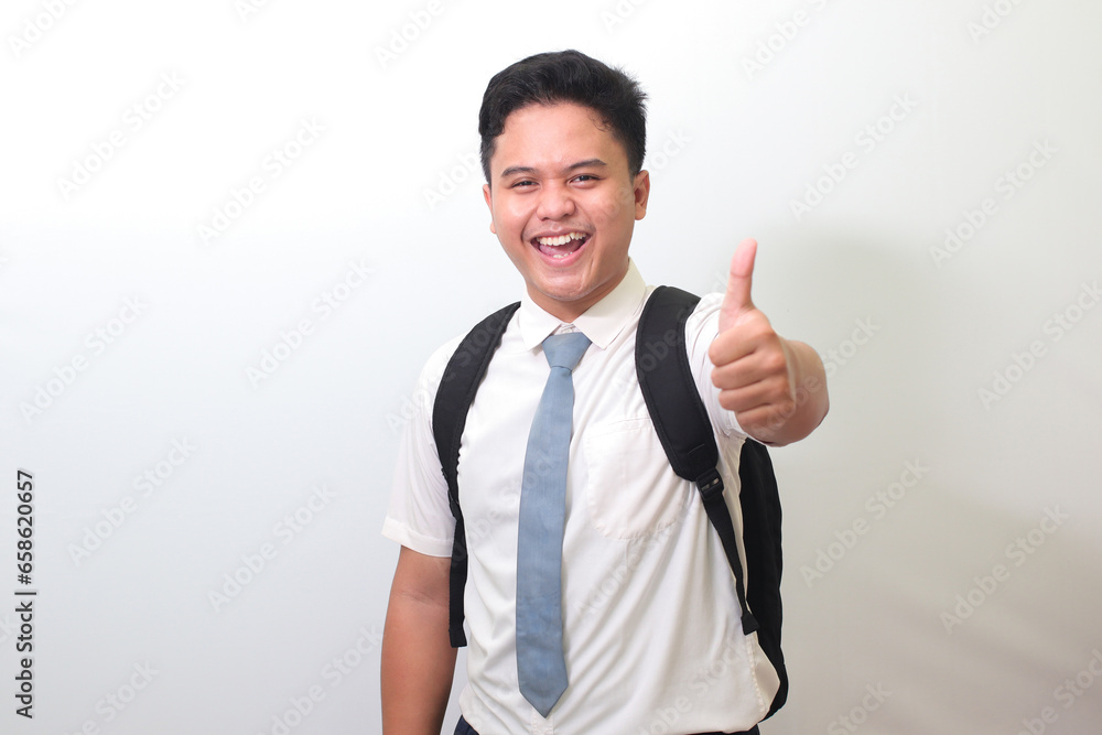 Indonesian senior high school student wearing white shirt uniform with gray tie smiling and looking at camera, making thumbs up hand gesture. Isolated image on white background Indonesian senior high school student wearing white shirt uniform with gray tie smiling and looking at camera, making thumbs up hand gesture. Isolated image on white background