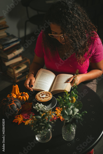 Girl reading book with Halloween cappuccino coffee with a scary spooky pumpkin latte art and decorations