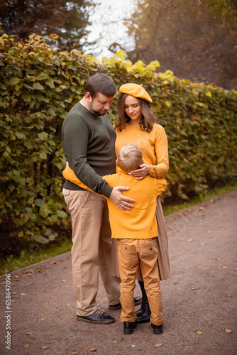 Mom, dad and son are standing hugging in an autumn park.