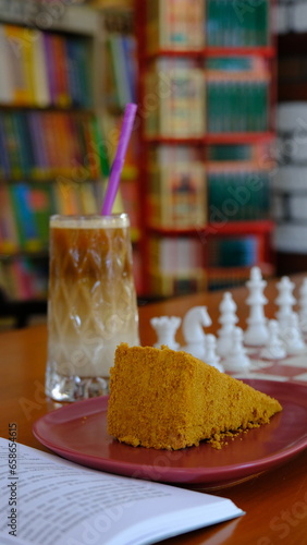 a slice of cake, a glass of cold coffee, book and chess board