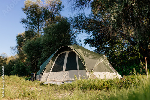 A green tent stands among beautiful nature on sunny days. Camping in summer