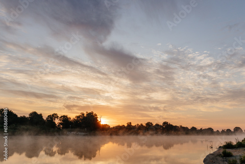 Beautiful landscape with a river and reflection, thick fog at dawn. Lake in the early morning in thick fog