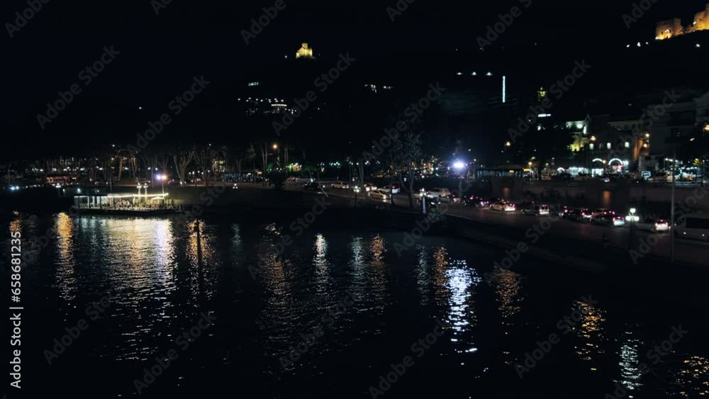 Cars driving on Kura river embankment. Illuminated Narikala fortress at background. Tbilisi night traffic Cars driving on Kura river embankment. Illuminated Narikala fortress at background. Tbilisi night traffic
