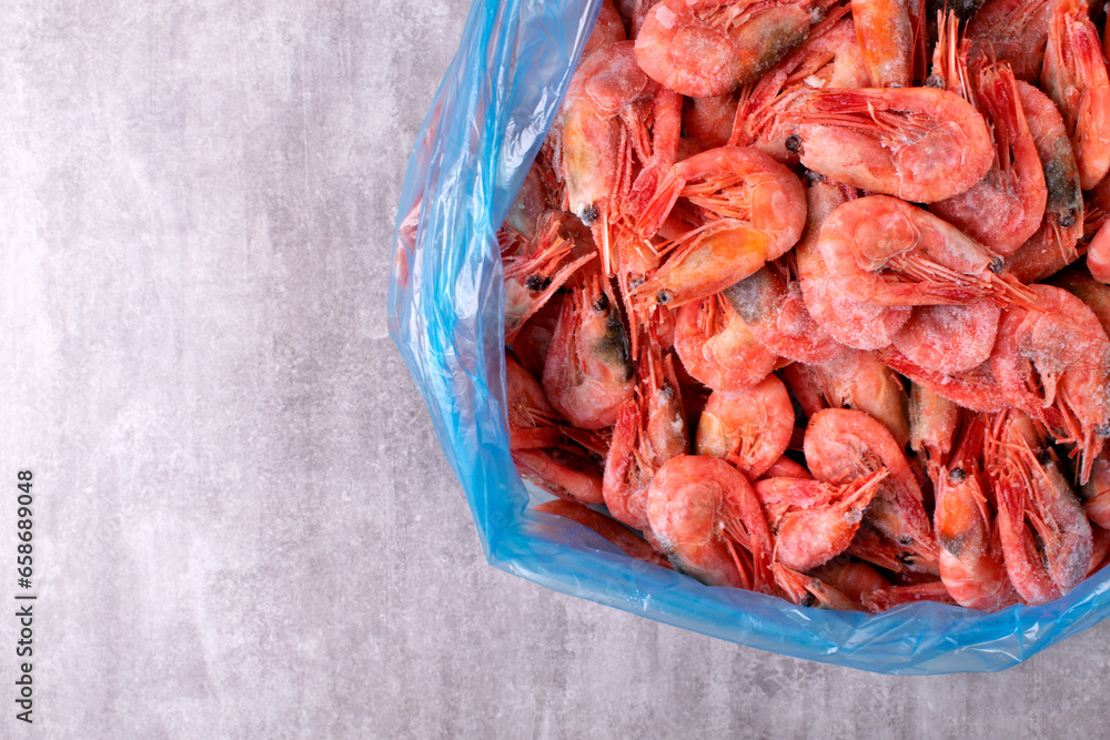 Frozen boiled shrimps in a plastic bag on gray table. Seafood product. Top view. Copy space