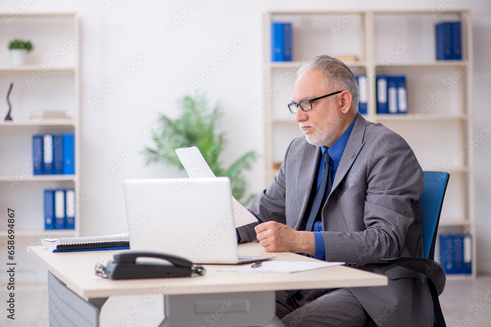 Old male employee reading paper at workplace Old male employee reading paper at workplace
