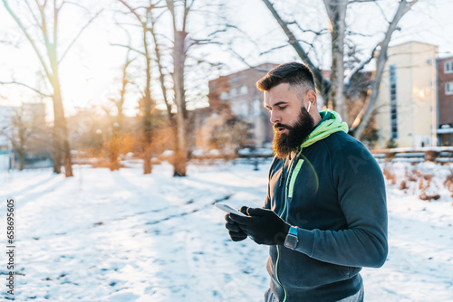 Handsome middle age man with a beard running and exercising outside on extremely cold and snowy day. Sport and fitness motivation theme. He using smart phone to track his activity data. © Dusko
