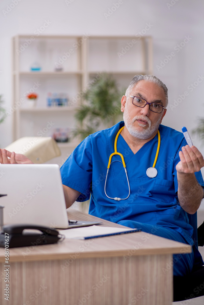 Old male doctor holding thermometer in the clinic Old male doctor holding thermometer in the clinic