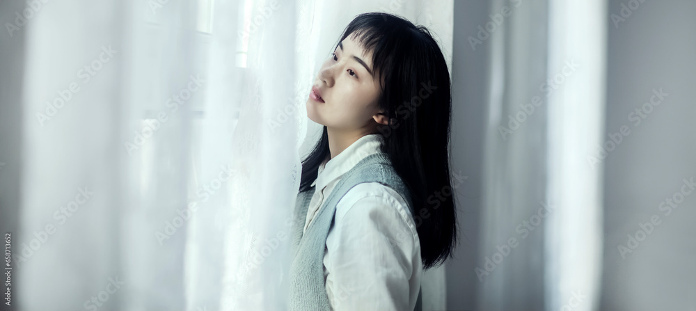 An autistic Asian girl leaning against the window - obrazy, fototapety, plakaty 