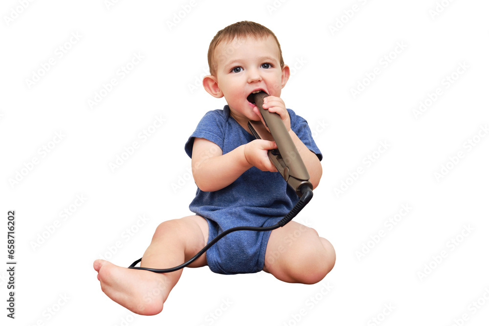 Child boy chewing on the electric wire of a curling iron, copy space, isolated on a white background. Toddler baby plays with hot curling tongs at the electrical outlet. Kid age one year Child boy chewing on the electric wire of a curling iron, copy space, isolated on a white background. Toddler baby plays with hot curling tongs at the electrical outlet. Kid age one year