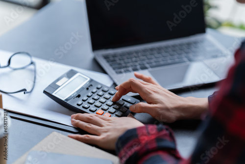 Business Documents concept: Employee woman's hands are working on calculator, notebook, laptop, and smartphone for searching and checking unfinished jobs.