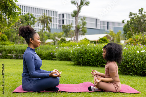 African American woman and her daughter in yoga suit are relaxingly practicing meditation exercise in the park to attain happiness from inner peace wisdom for healthy mind and soul concept photo