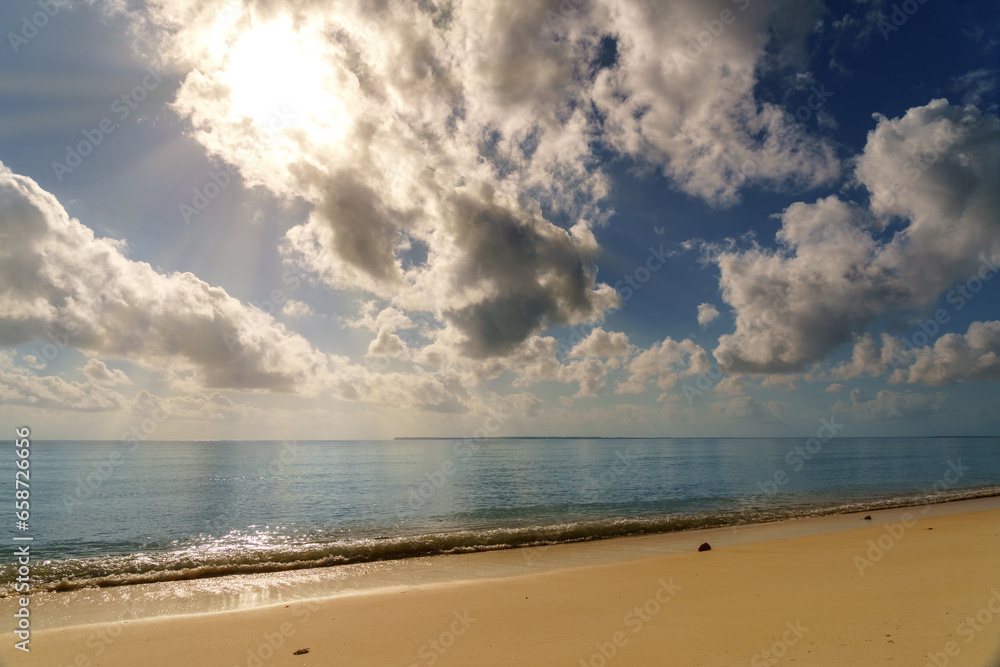 sunny blue skies calm ocean water with clouds and a flat sand coastline beach.