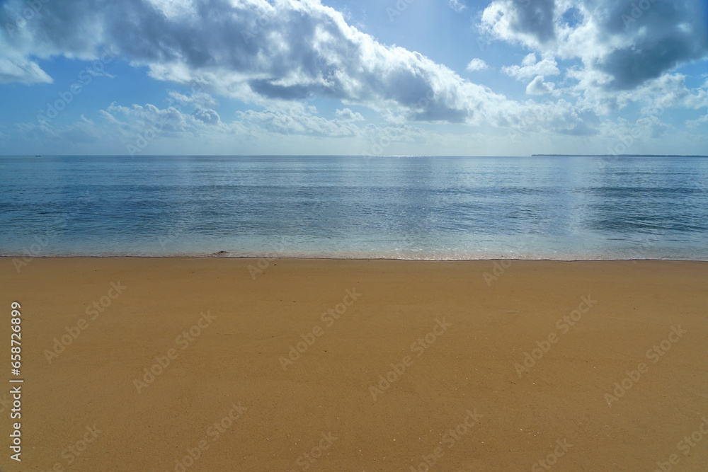 sunny blue skies calm ocean water with clouds and a flat sand coastline beach.