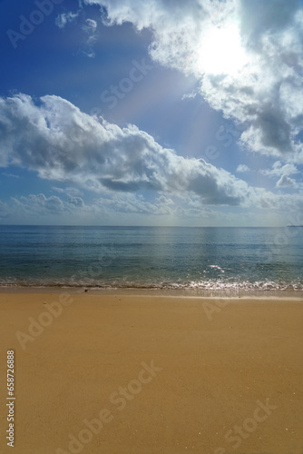 sunny blue skies calm ocean water with clouds and a flat sand coastline beach.