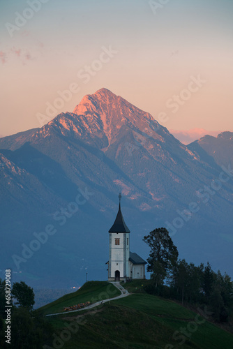 Sunset over The Church of St. Primoz and Felicijan in the village of Jamnik. The last ray of sun on the Alps in Slovenia. Vertical view.