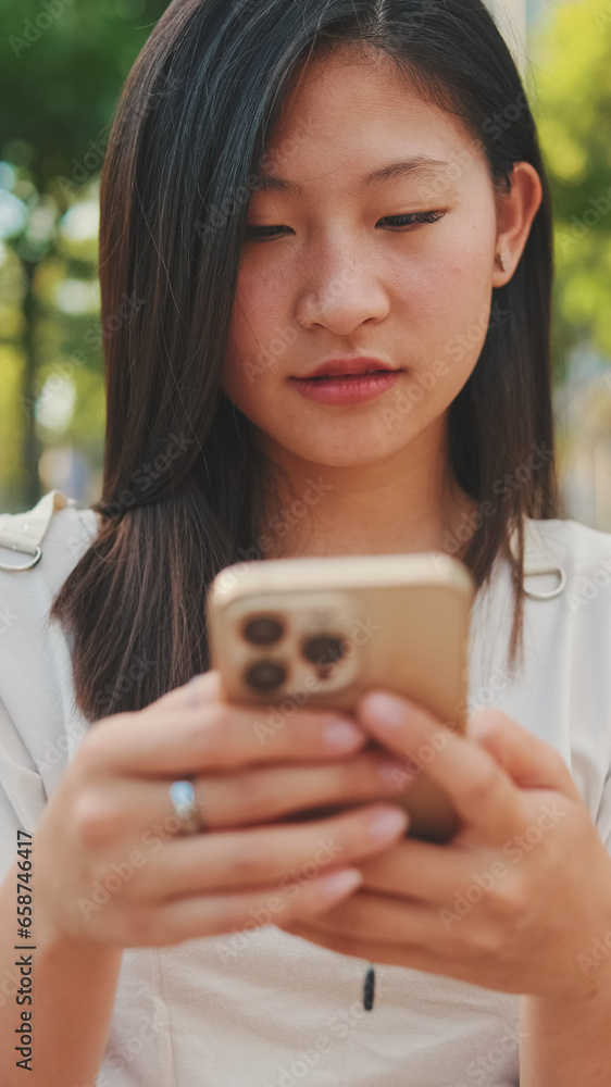Close up, beautiful brunette girl sitting on bench in city park, using phone with mobile app, surfing social media, checking news Close up, beautiful brunette girl sitting on bench in city park, using phone with mobile app, surfing social media, checking news
