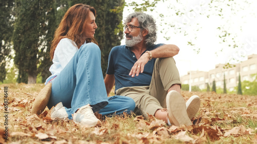 Retired couple talking, sitting on the grass in the park in autumn