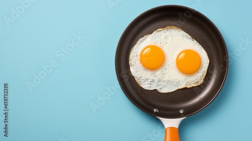 Top view of a fried egg on a blue frying pan next to uncooked whole eggs and eggshells in darkness, isolated on an orange background.