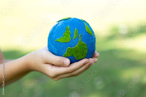 Young boy's hand holding planet Earth globe at natural park background as Earth day to save this planet with ESG principle and environment friendly energy for brighter future. Gyre