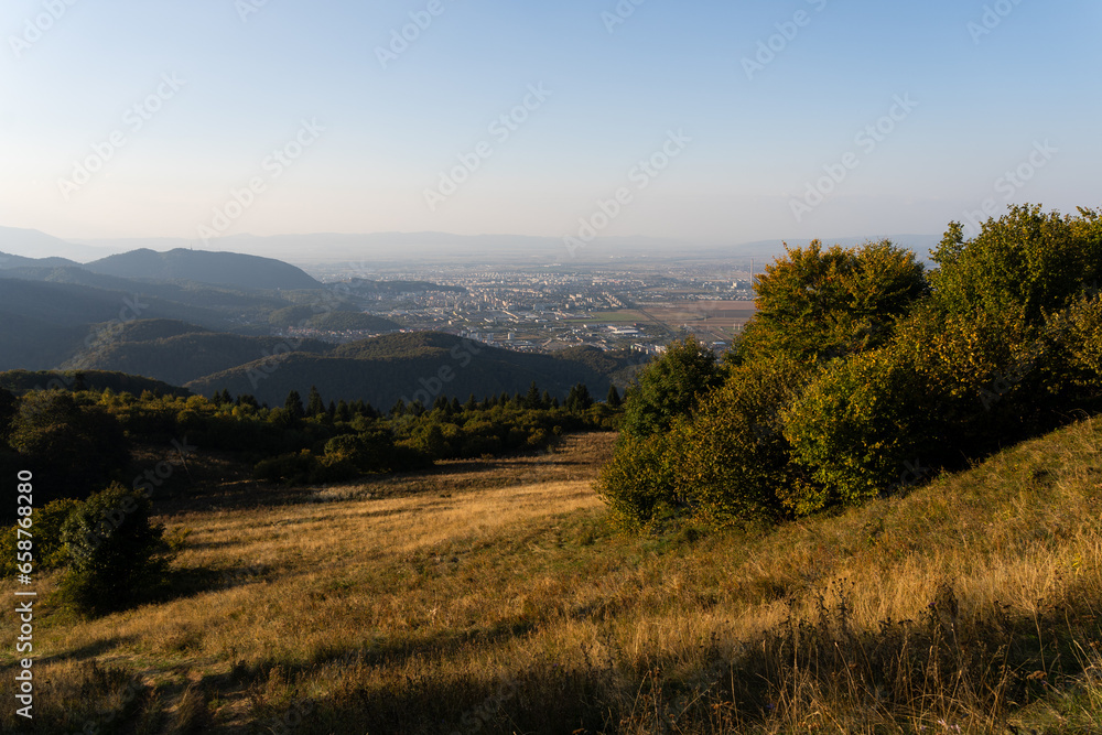 Calm view from the top of the hill to Sacele town in Romania from Piatra Mare mountain with a golden autumn grass and green forest