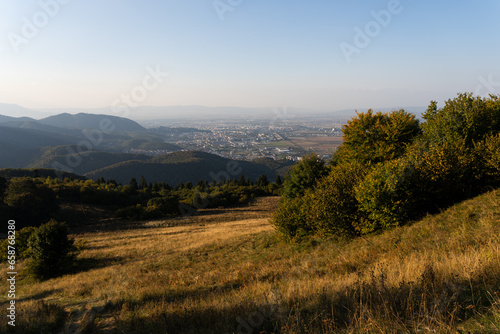 Calm view from the top of the hill to Sacele town in Romania from Piatra Mare mountain with a golden autumn grass and green forest